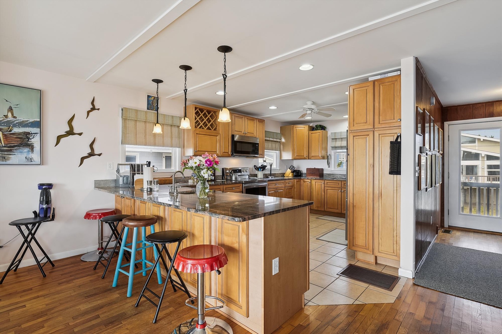You'll love gathering at the spacious granite breakfast bar, where colorful stools invite casual meals and morning coffee in this bright, fully-equipped kitchen with warm wood cabinetry.