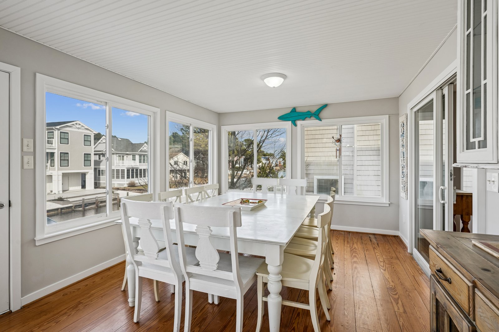 Your bright dining room features a charming white table surrounded by windows that flood the space with natural light and coastal views.