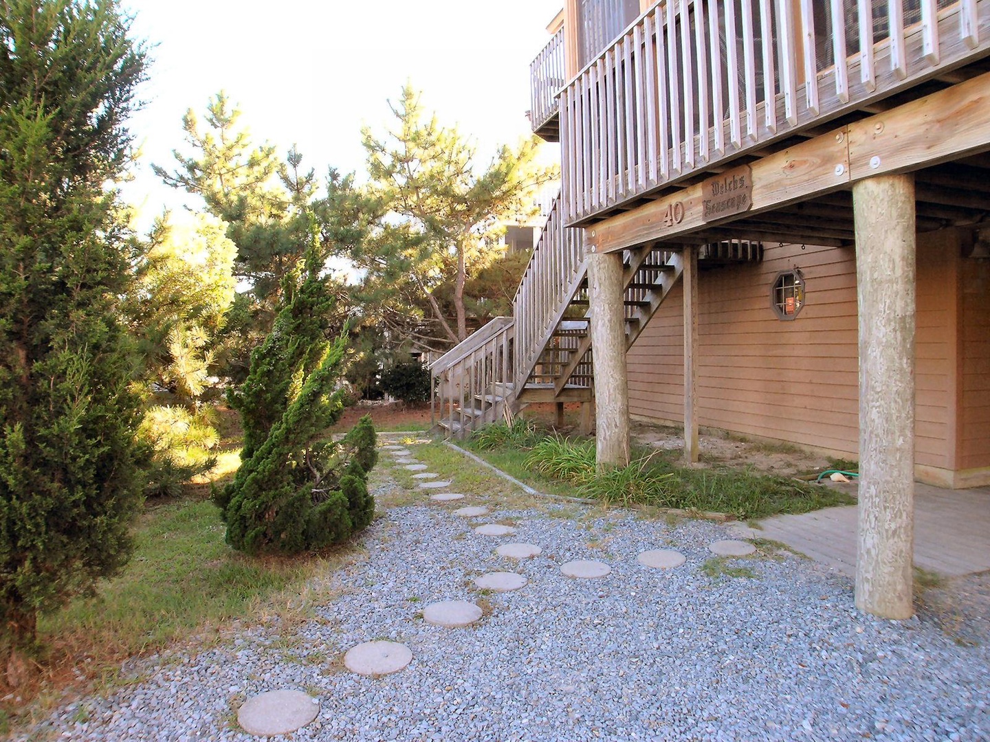 A charming coastal cottage with weathered wood siding, elevated deck, and stepping stone pathway through native landscaping creates a serene beach retreat atmosphere.
