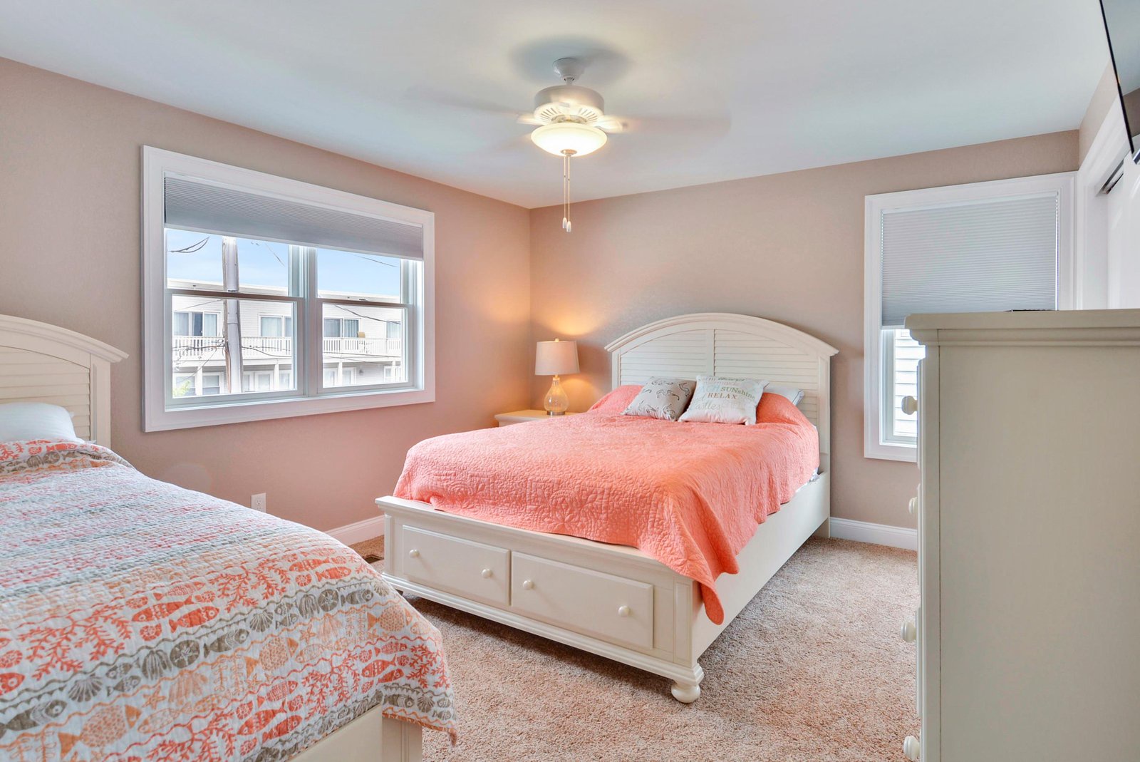 Drift off to sleep in this welcoming bedroom adorned with warm coral and soft white hues. With two cozy beds and ocean breezes through your windows, restful nights await.
