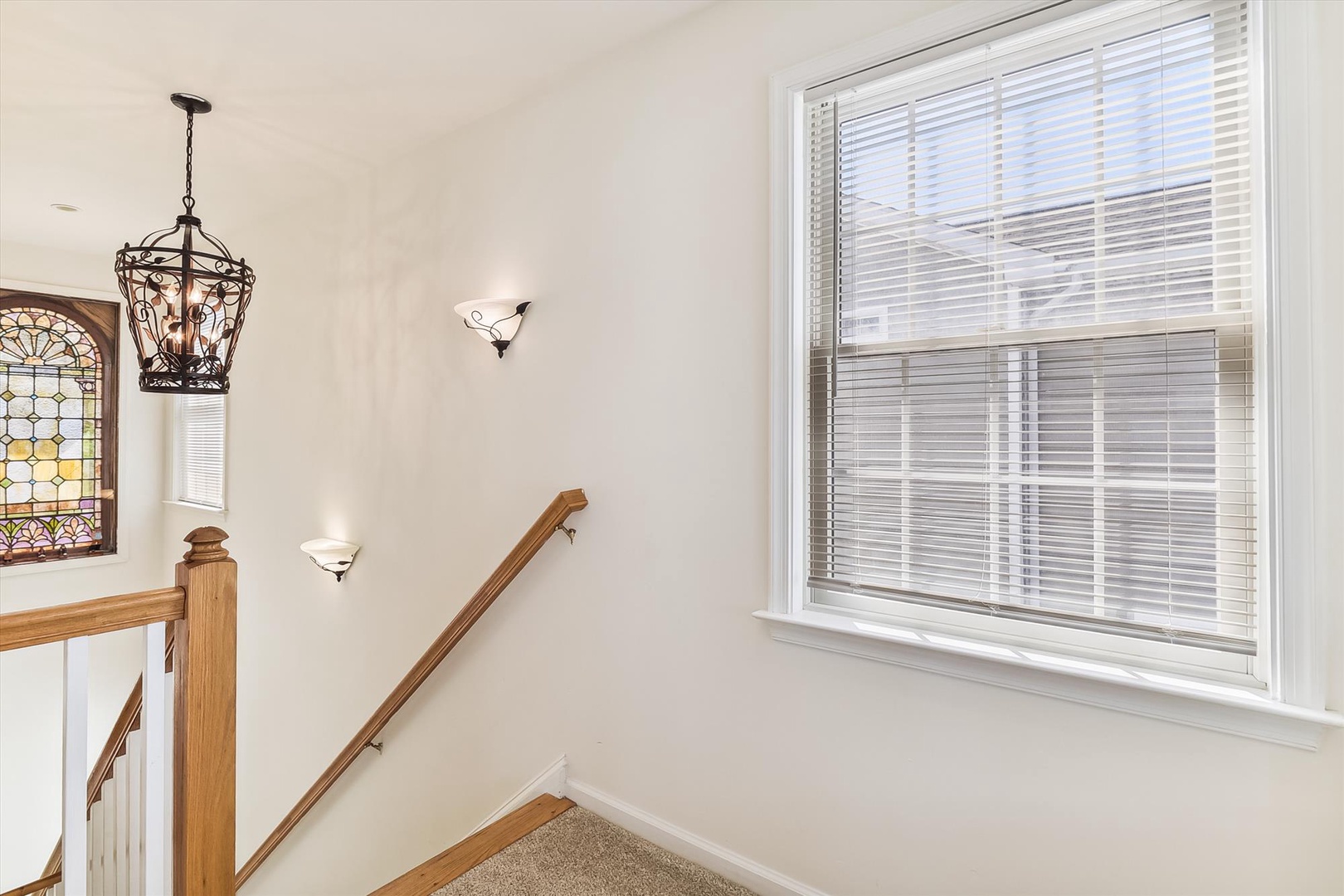 Bright and airy staircase landing with elegant pendant lighting, decorative stained glass window, and wooden handrail details welcoming you upstairs.