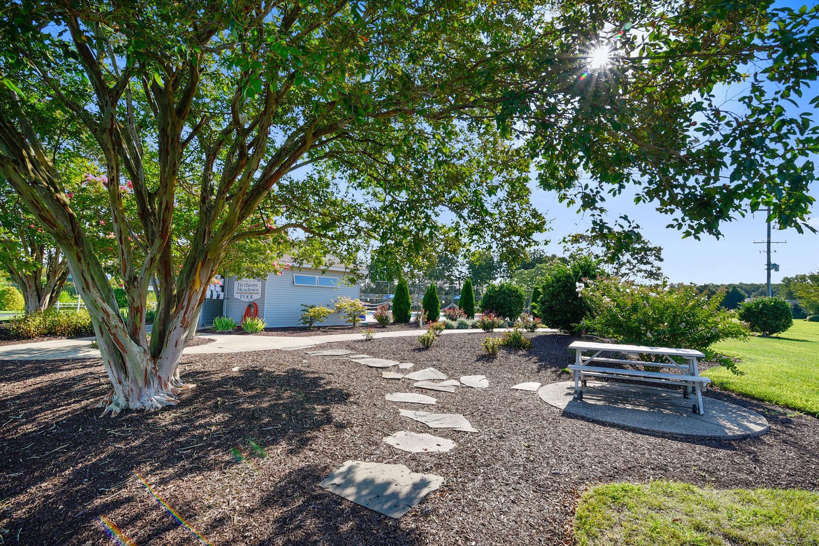 The property's landscaped grounds feature mature trees providing natural shade, a stone pathway leading to the main building, and peaceful outdoor seating areas perfect for relaxation.