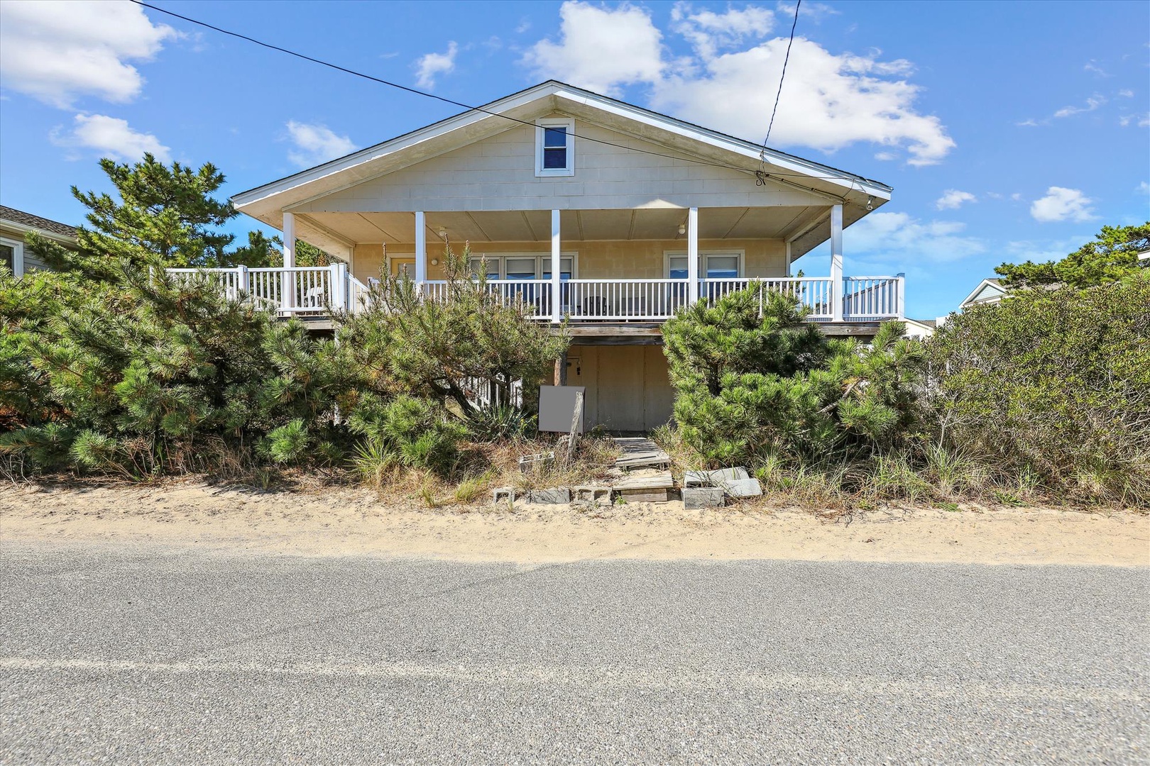 Elevated beach house with spacious covered porch, nestled among coastal vegetation and just steps from the sandy shore.