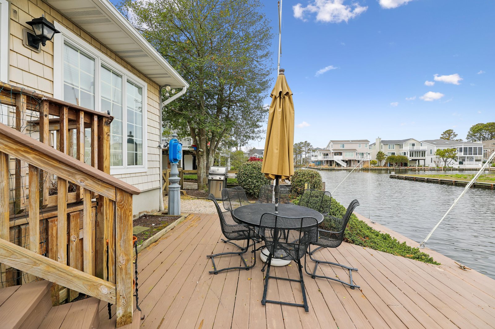The property features a private deck overlooking a tranquil canal, with waterfront homes visible across the water and a peaceful residential setting offering a coastal escape.