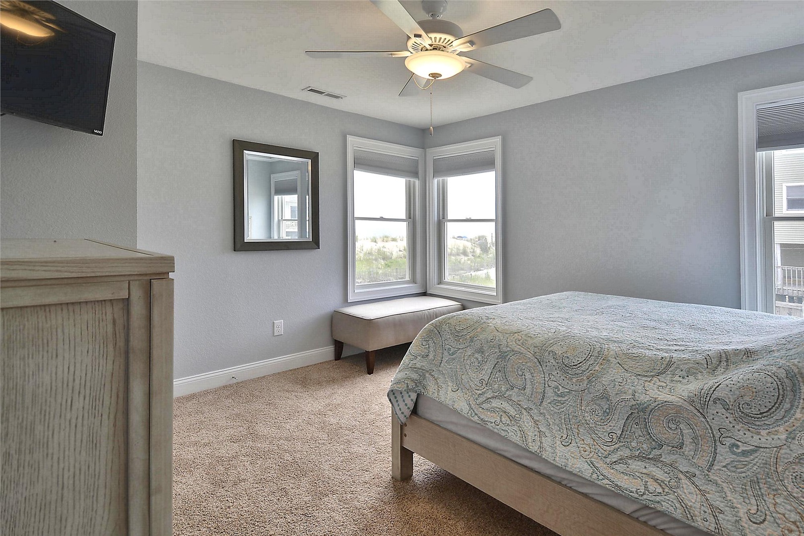 Drift off in this serene bedroom with a plush bed, calming coastal tones, and a ceiling fan for your comfort. Wake up to natural light streaming through large windows framing lovely views.