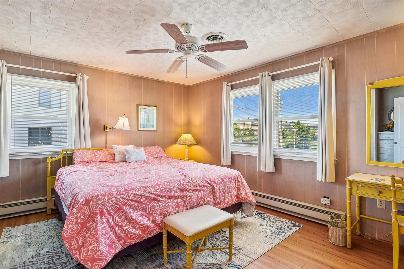 Sink into soft linens in this cheerful bedroom, where wood-paneled walls and sunny accents create a cozy coastal vibe. Wake refreshed with natural light streaming through your windows and a ceiling fan keeping you comfortable year-round.
