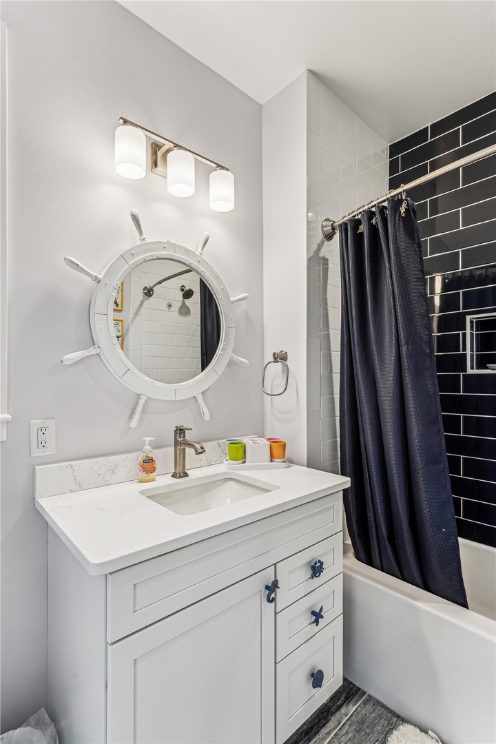 Step into your charming nautical bathroom with ship's wheel mirror and crisp white vanity for refreshing coastal vibes.