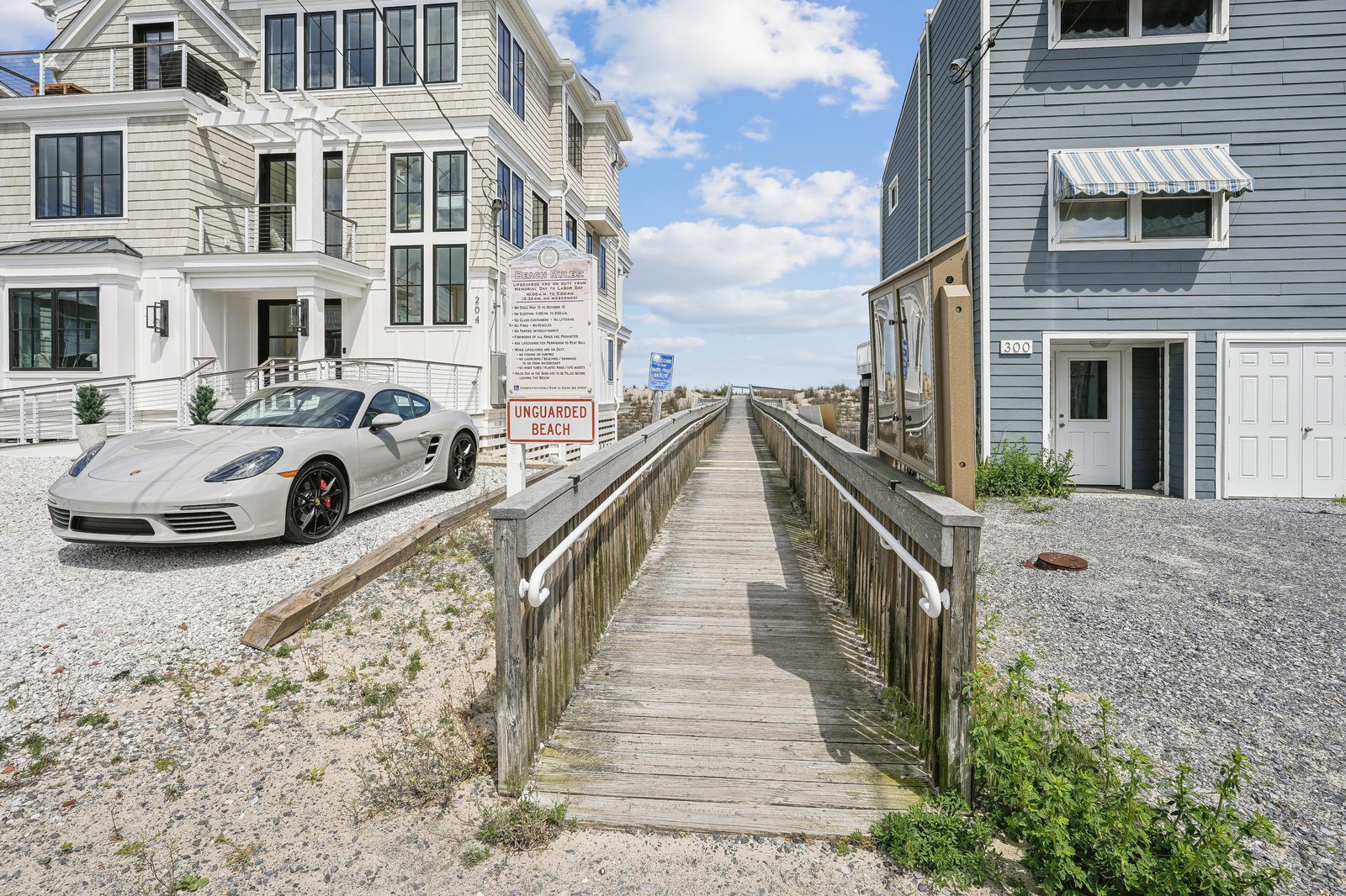 Oceanfront properties with direct boardwalk access leading to an unguarded beach area, set in a coastal neighborhood of modern beach homes.
