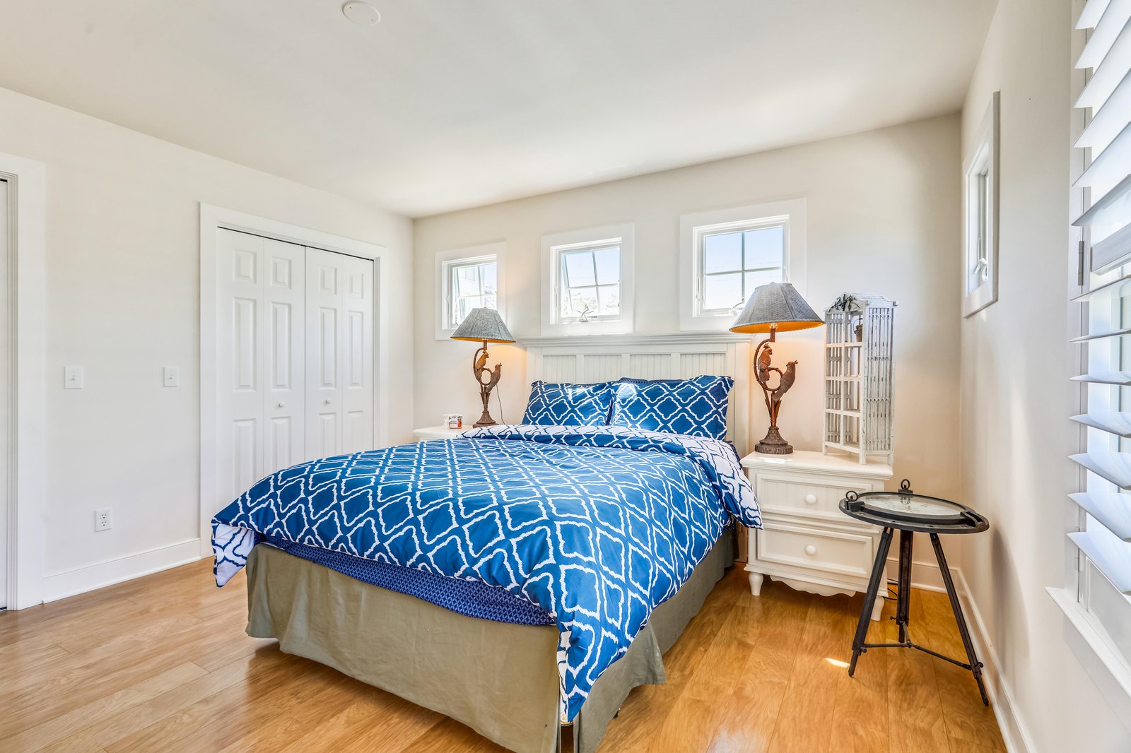 Your bright coastal bedroom features a cozy queen bed with vibrant blue linens, charming nautical lamps, and sunlight streaming through the windows. Relax in this peaceful retreat after a day of adventure.