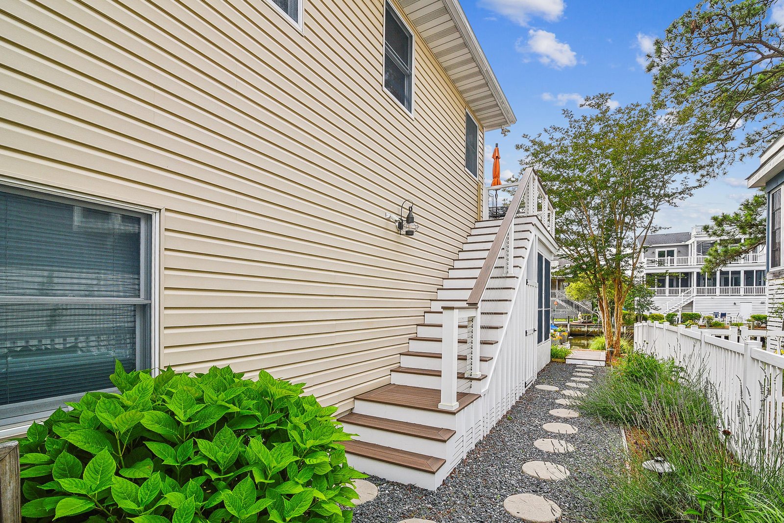 The property sits in a well-maintained residential neighborhood with easy access from a charming walkway bordered by lush greenery and coastal landscaping.