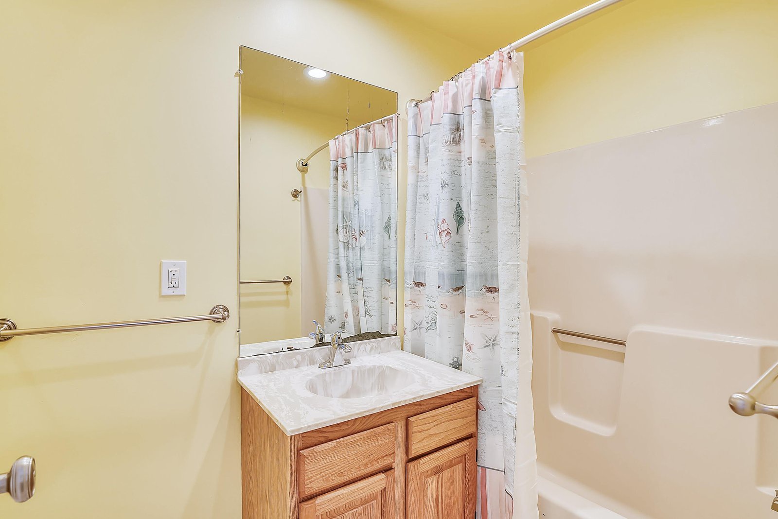 Your private bathroom features a tub-shower combo with a cheerful coastal-themed curtain, plus handy grab bars for added comfort and safety. The marble-topped vanity and bright mirror make getting ready a breeze.