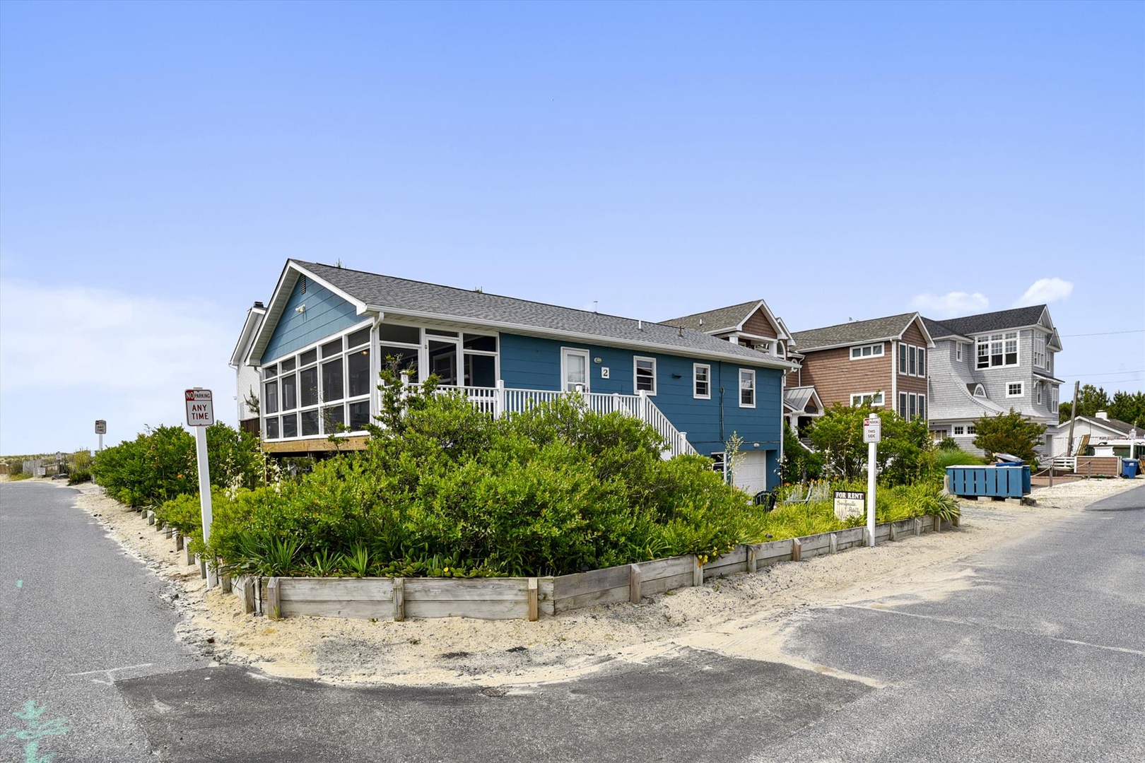 A charming coastal beach house with a screened porch and natural landscaping, nestled in a quiet beachside neighborhood. The elevated design is typical of coastal properties.