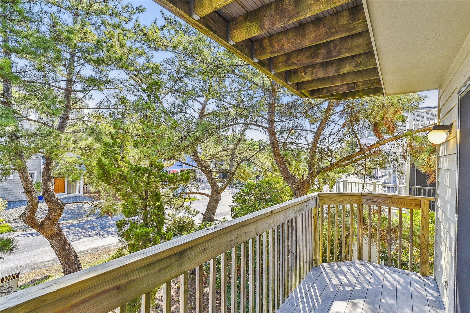 A covered balcony with wooden details frames serene views of coastal trees and the surrounding neighborhood, offering a peaceful retreat for morning coffee or evening relaxation.