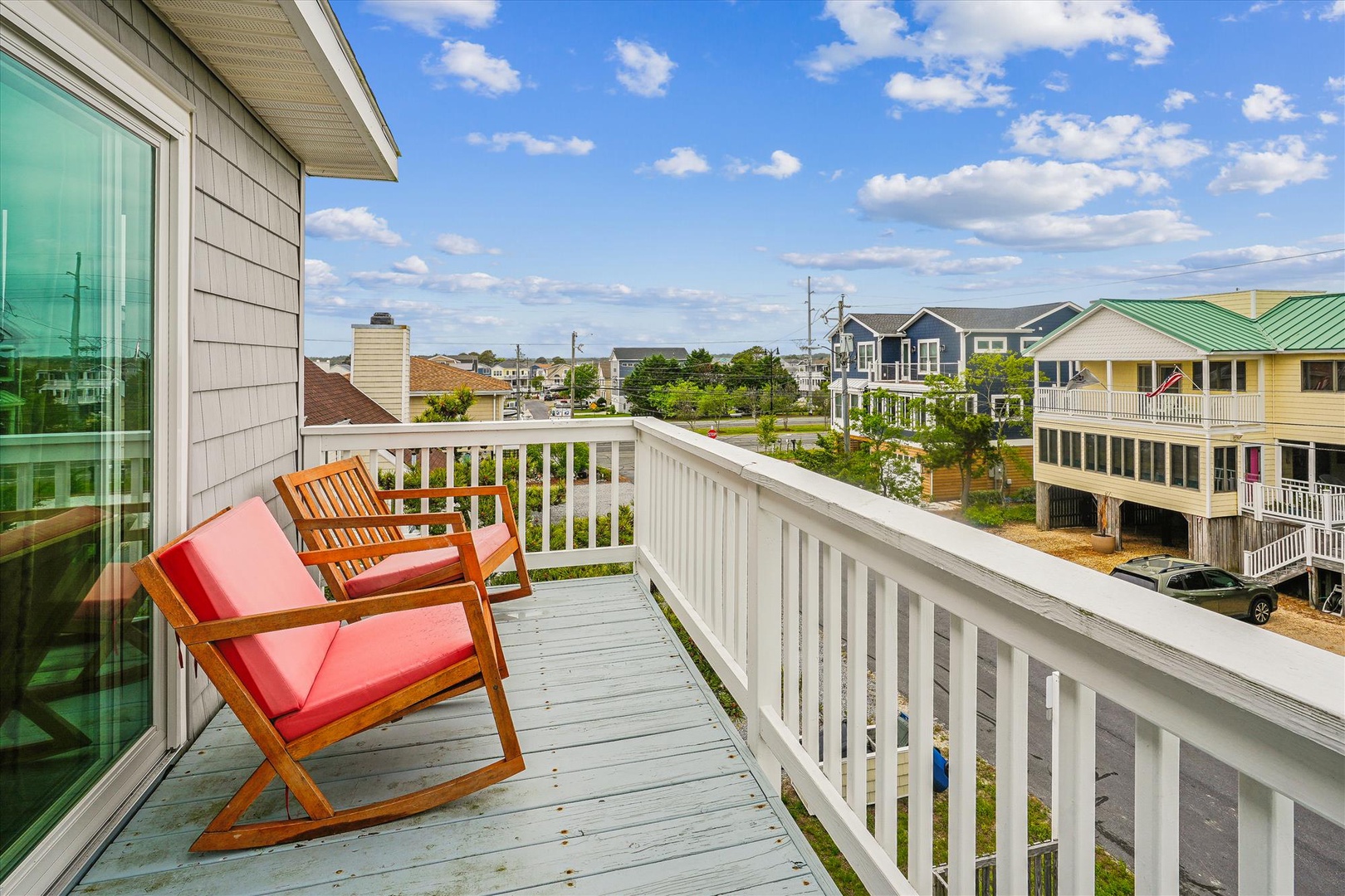 A peaceful neighborhood view from the property, featuring colorful residential homes and a clear blue sky with scattered clouds.