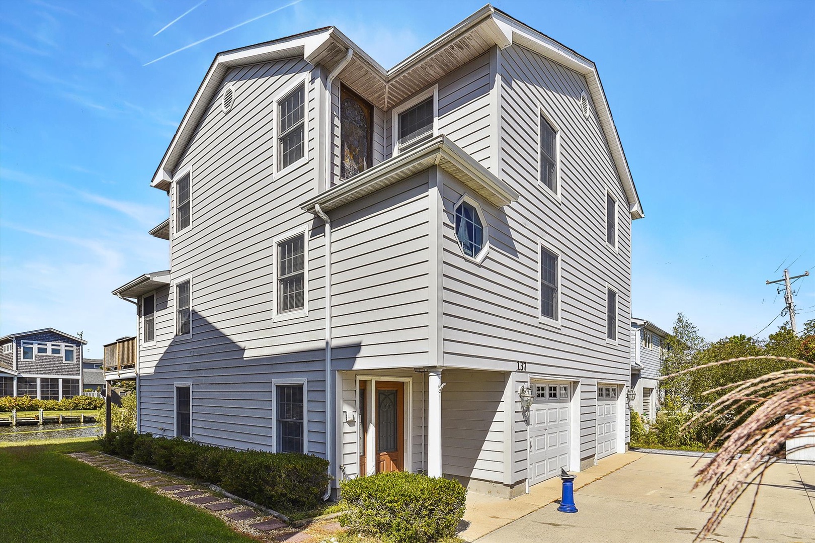 A spacious three-story coastal home with clean white siding and multiple windows, featuring covered parking and landscaped grounds in a quiet residential neighborhood.