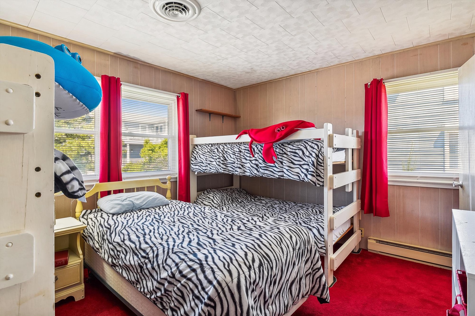 Perfect for families, this fun bedroom features a cozy bunk bed with zebra-striped bedding and bright red curtains framing leafy views. The kids will love claiming their favorite bunk!