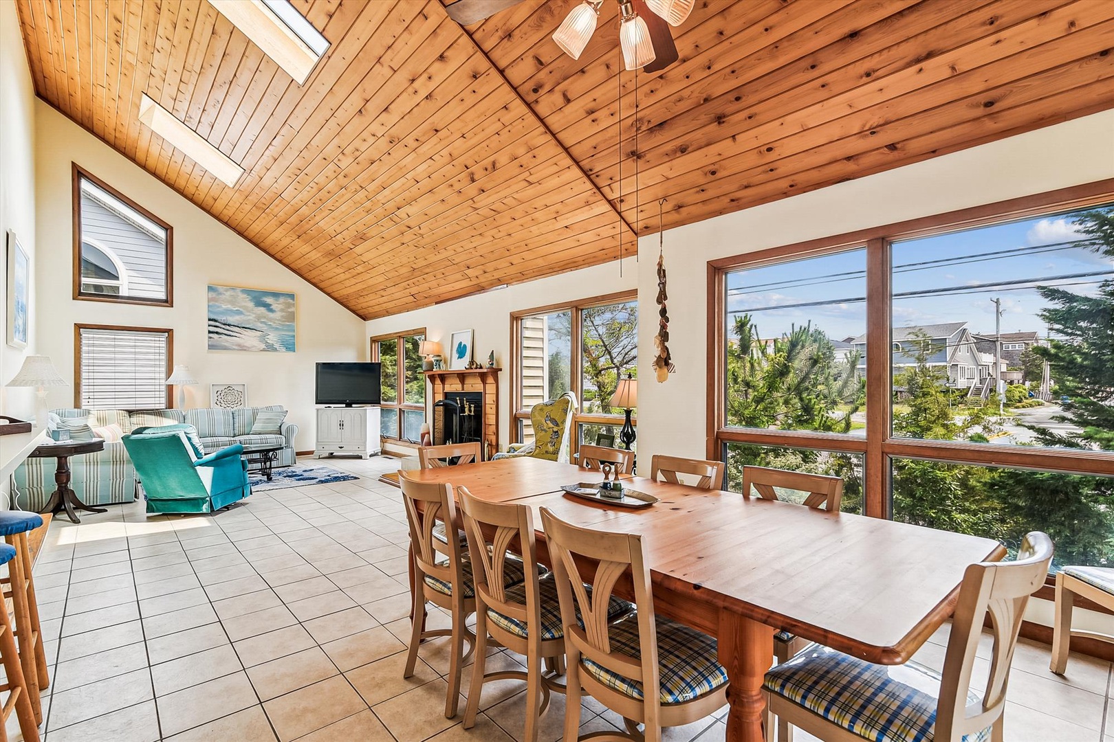 A light-filled living and dining space with vaulted wood ceilings, skylights, and expansive windows overlooking the neighborhood. Gather around the spacious dining table or relax in the cozy seating area.