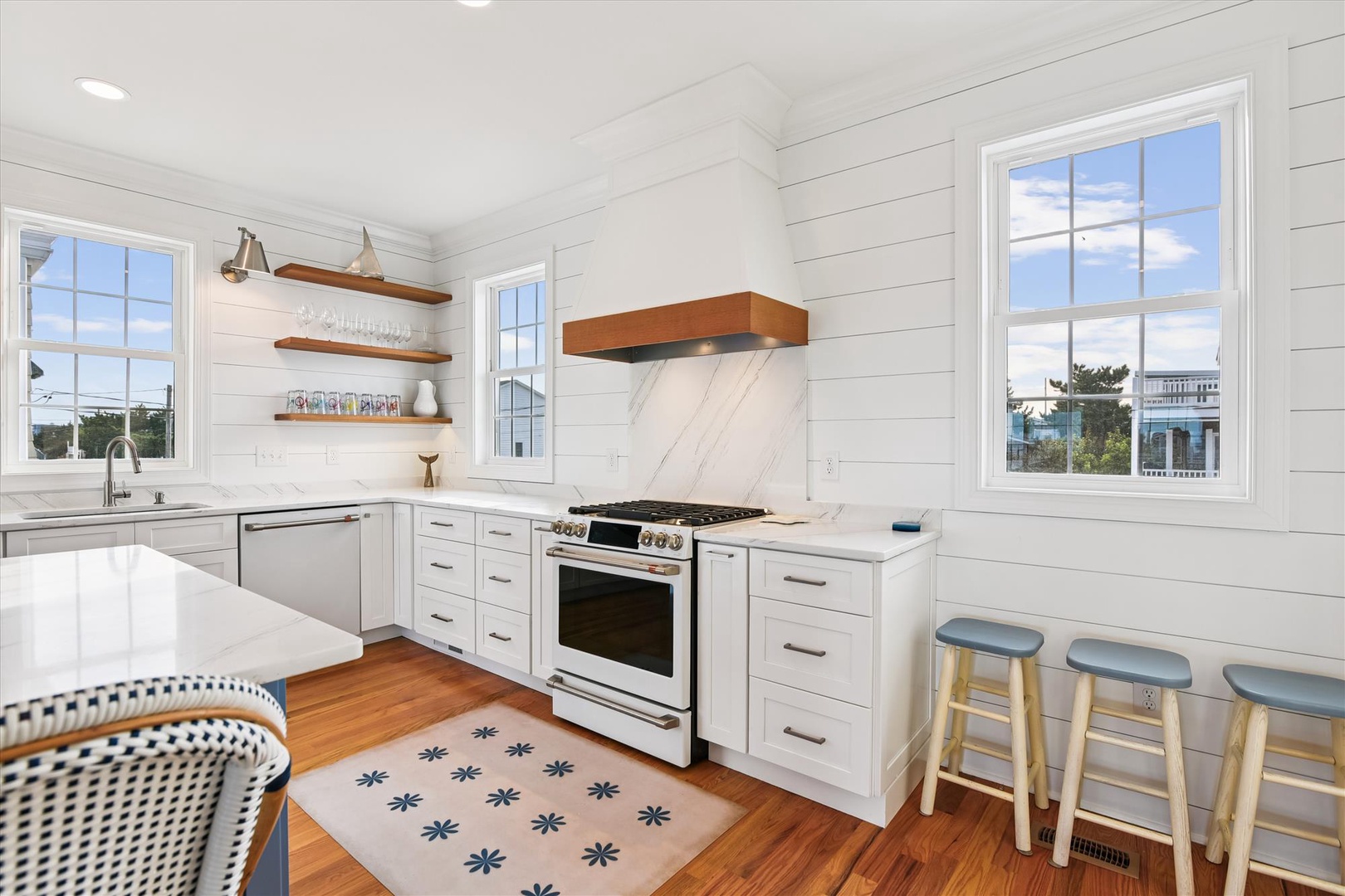 Your kitchen is a coastal dream: shiplap walls, marble backsplash, stainless appliances, and bar seating beneath sunny windows. Cook, gather, and feel right at home in this bright space.