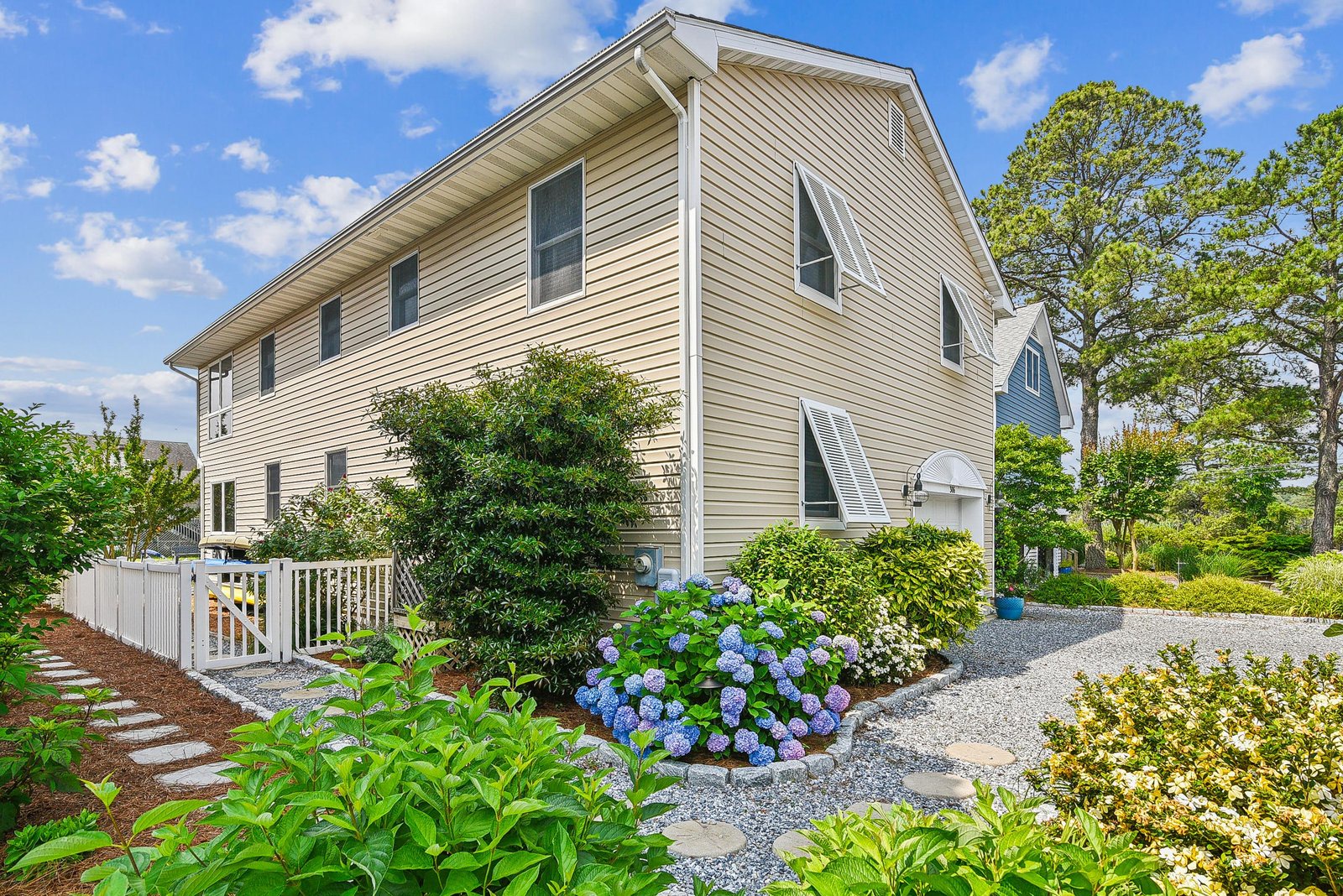 A charming two-story property features a welcoming exterior with clean siding and thoughtful landscaping. Mature trees surround the home, and vibrant hydrangeas line the pathway, creating a peaceful arrival experience in a lush, scenic neighborhood.