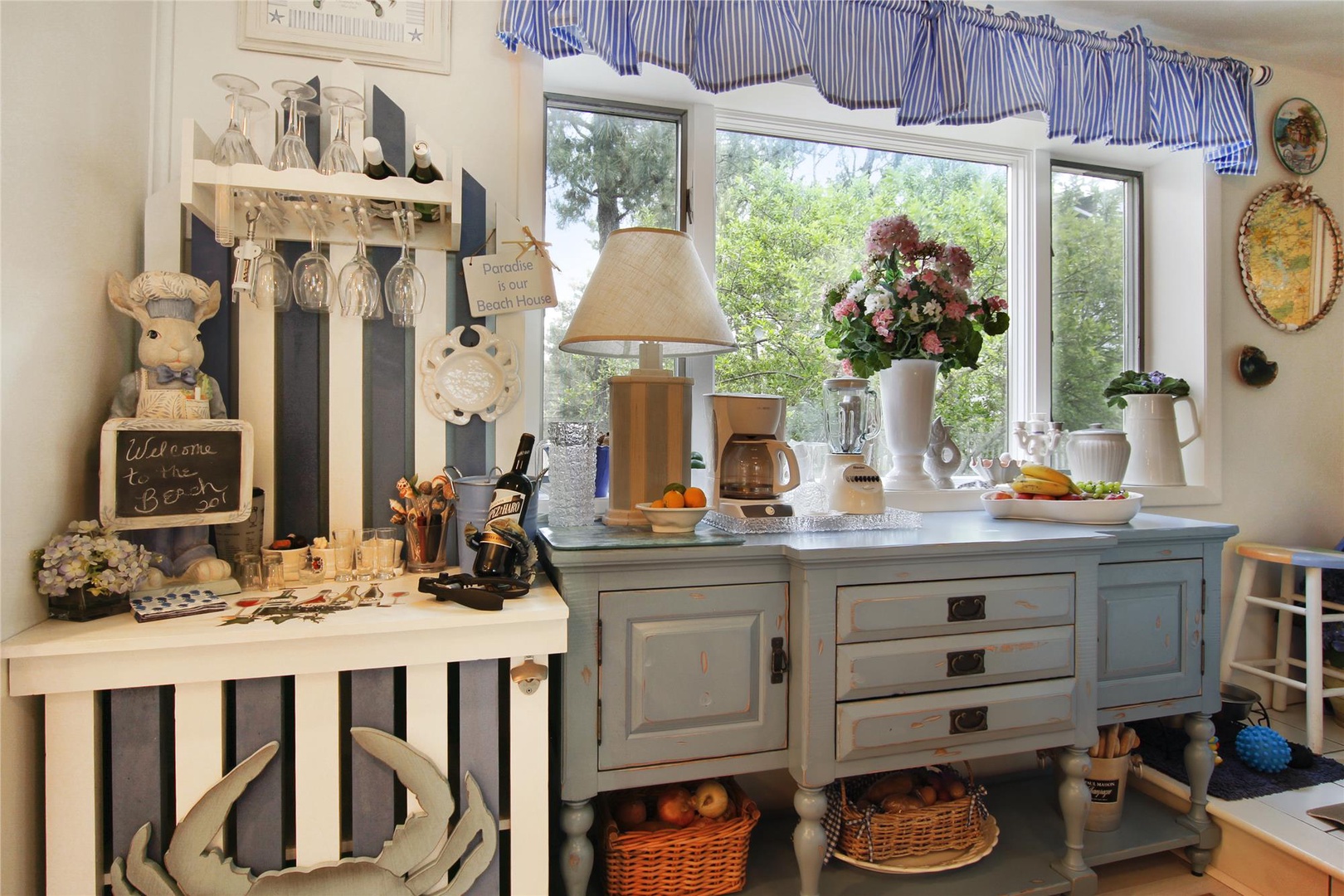 Sunlight pours through your kitchen window onto the charming sideboard, where fresh flowers and thoughtful touches create a welcoming coastal atmosphere.