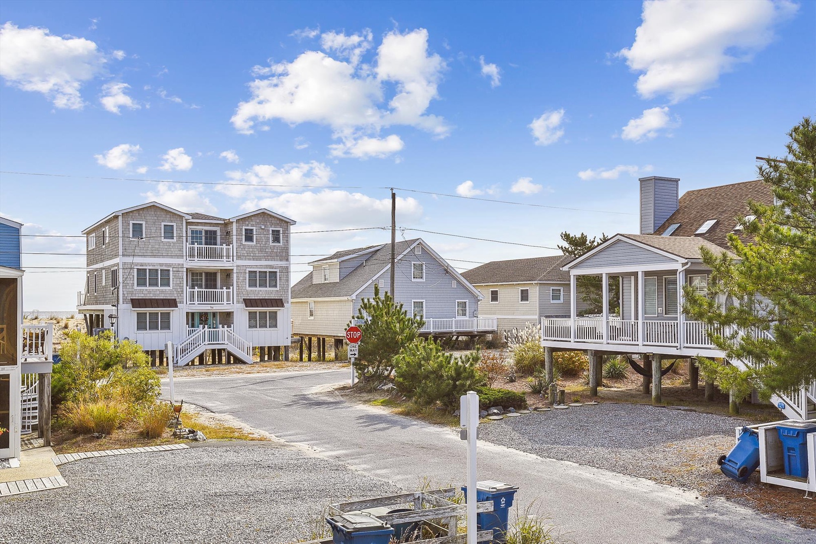 A quiet coastal neighborhood with stilted beach homes, featuring parking and landscaped yards beneath sunny skies. Perfectly positioned for easy beach access.