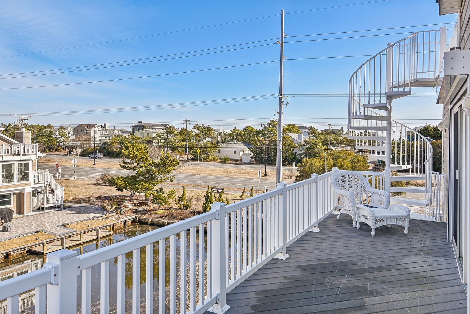 This spacious deck offers an elevated outdoor retreat with white wicker seating and a spiral staircase leading to even more outdoor space. The quiet neighborhood setting provides a peaceful backdrop for morning coffee or evening relaxation.
