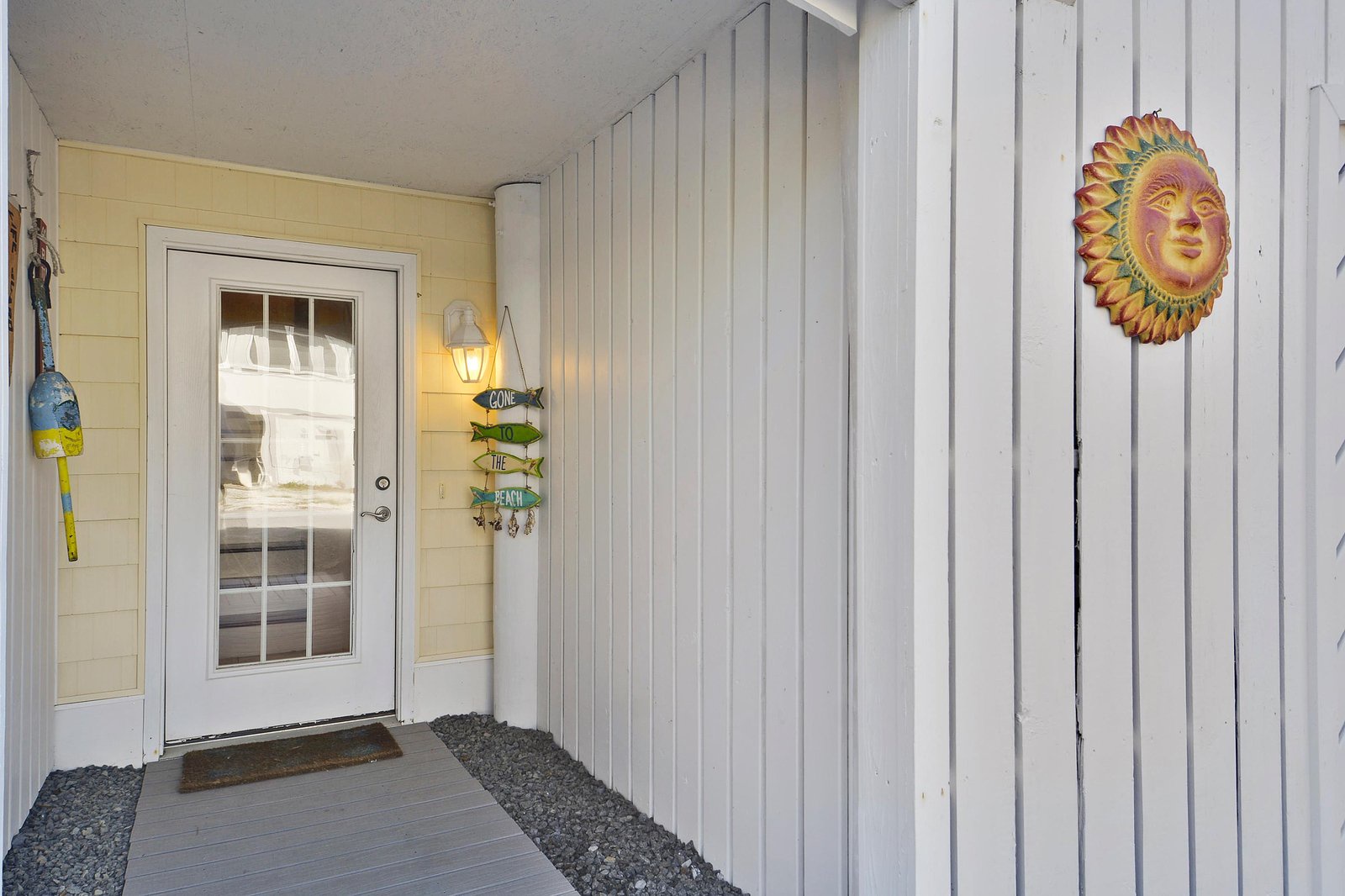 A cheerful sun decoration welcomes you at the covered entrance, where coastal charm meets practical shelter from the elements.