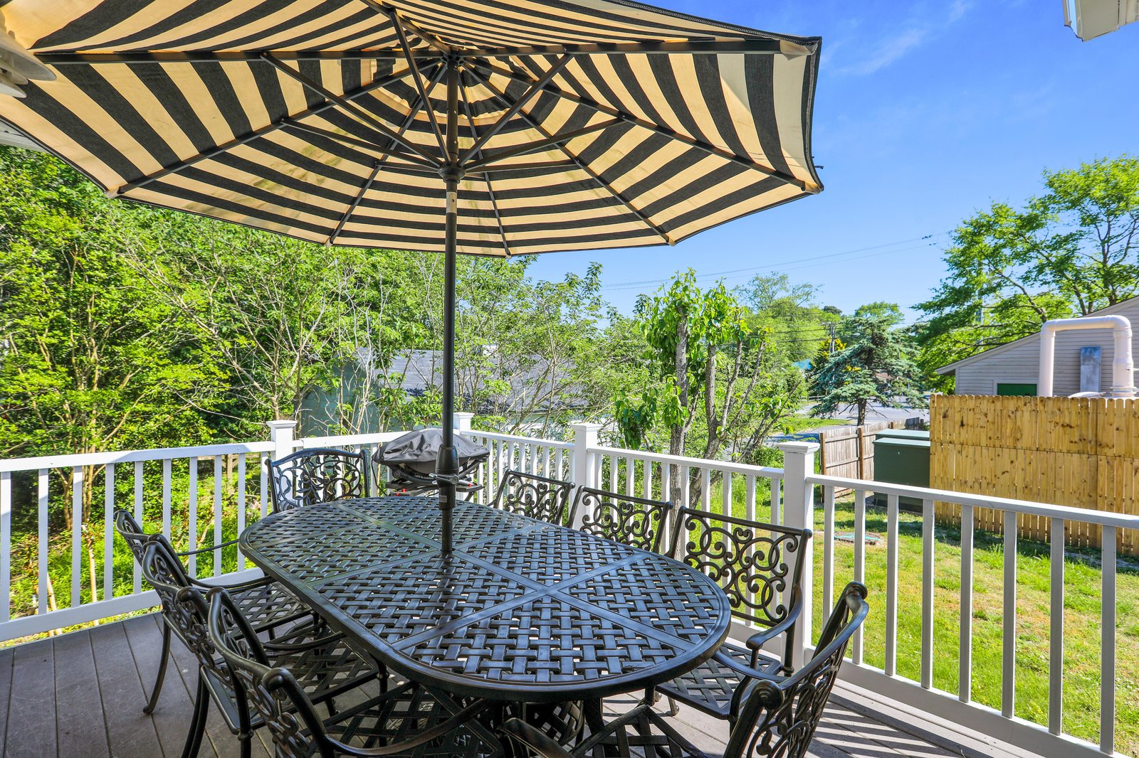 Your private deck invites leisurely meals under a cheerful striped umbrella, with lush greenery all around and sunny skies overhead.