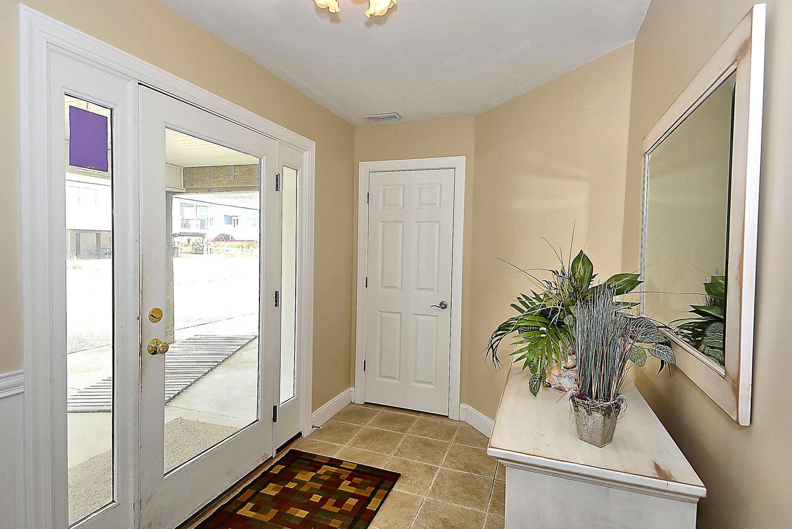 This welcoming entryway features bright natural light, clean tile flooring, and a stylish accent table with fresh greenery—making your arrival feel inviting from the first step inside.