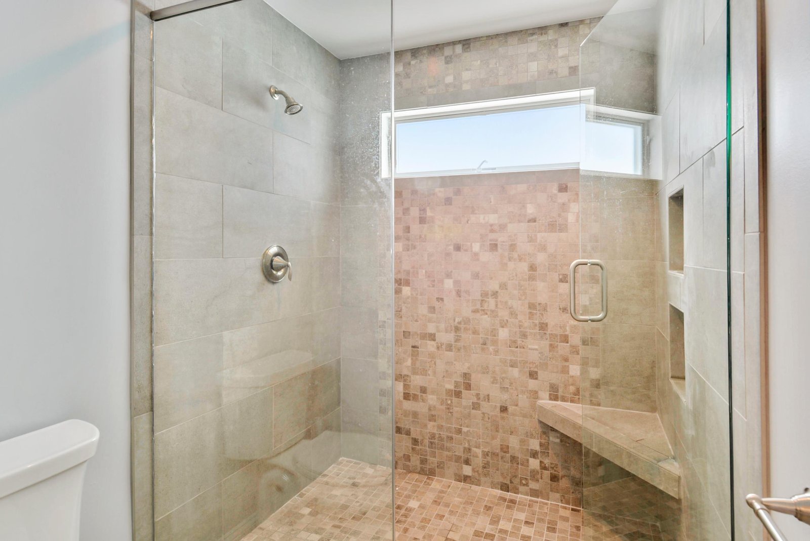 Step into your spa-like walk-in shower, where elegant mosaic tiles and a built-in bench invite you to unwind. Natural light streams through the window, making your morning routine feel luxurious and refreshing.