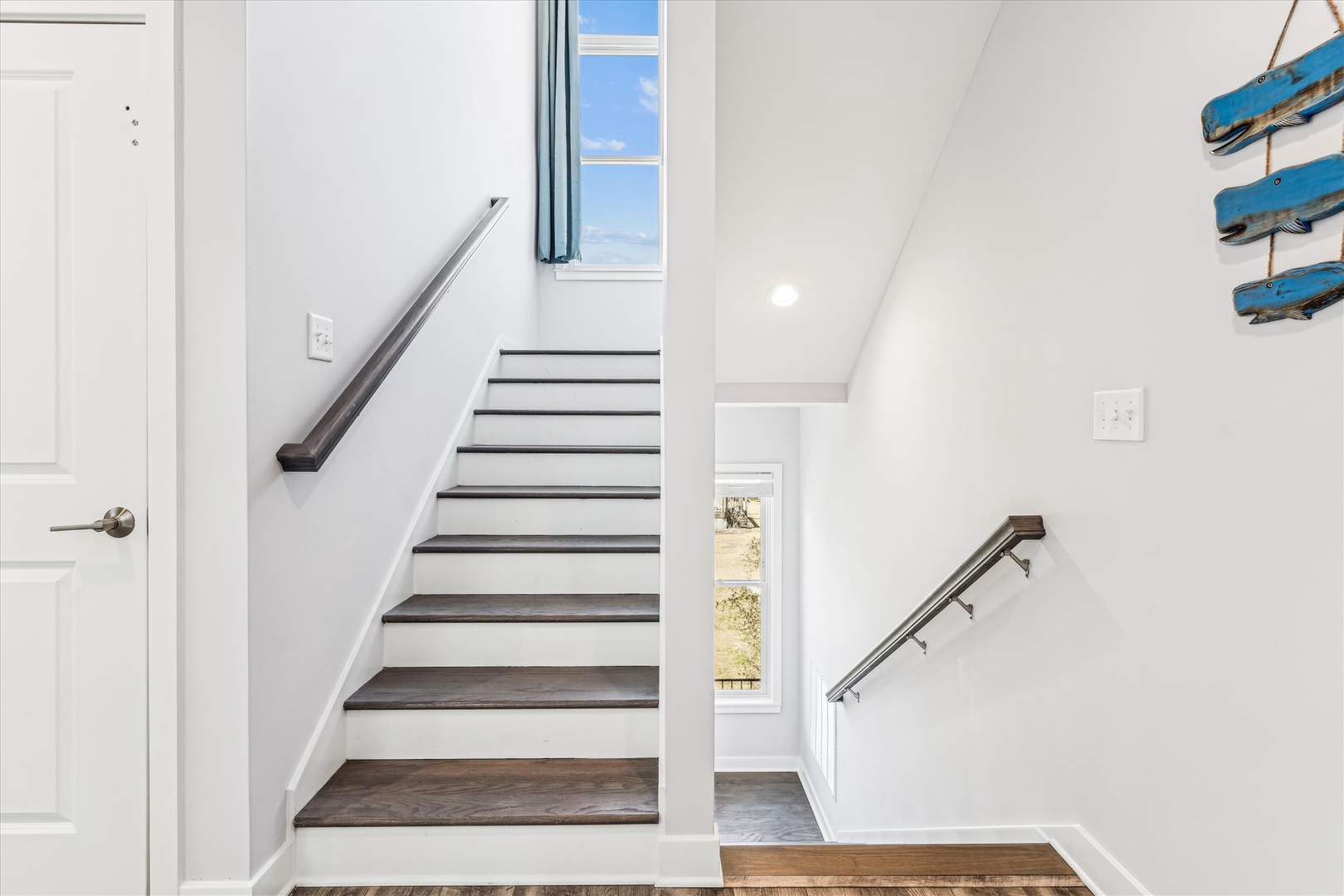 Bright staircase with coastal charm and hardwood flooring, leading you upstairs where natural light pours in through the windows at every turn.