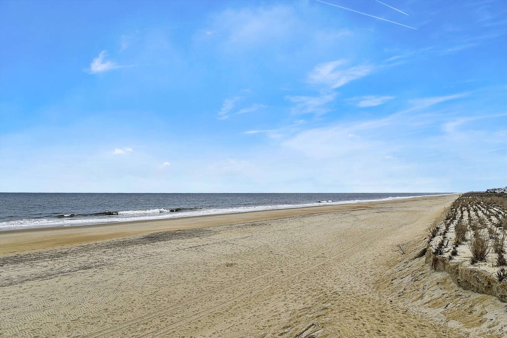 A wide, pristine beach with soft sand stretches along calm waters under clear blue skies, part of the surrounding coastal area near the property.