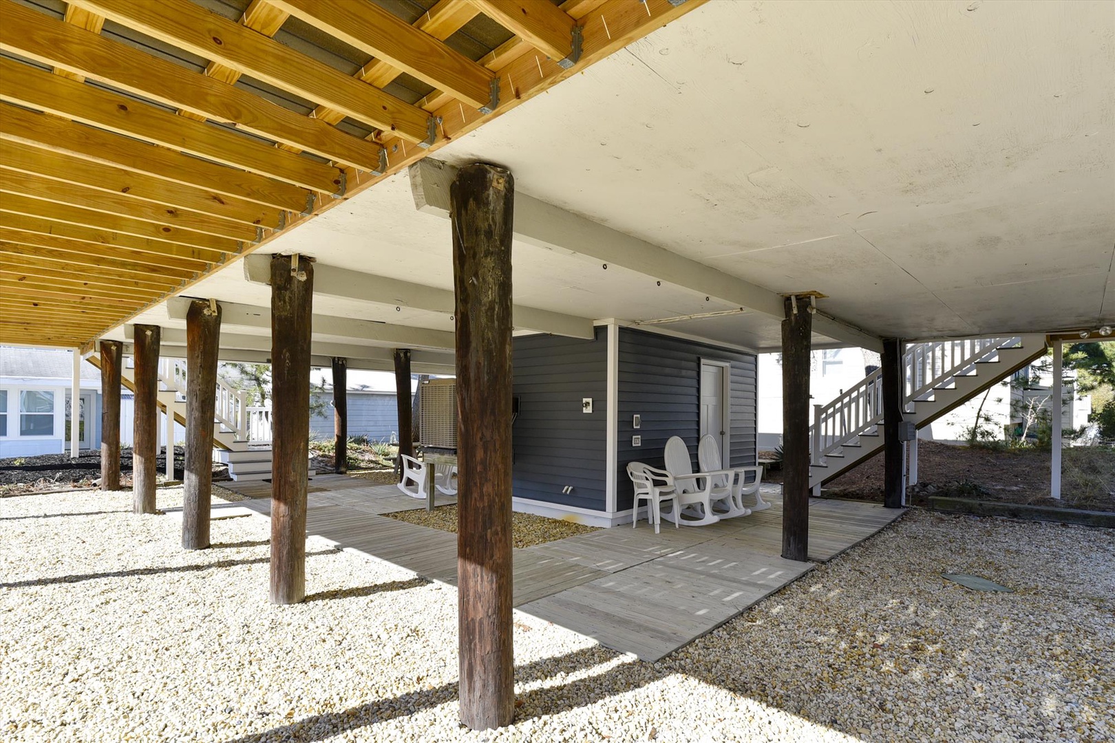 Spacious covered ground-level area with rustic wood beam construction, elevated seating space, and staircase access to main living quarters.
