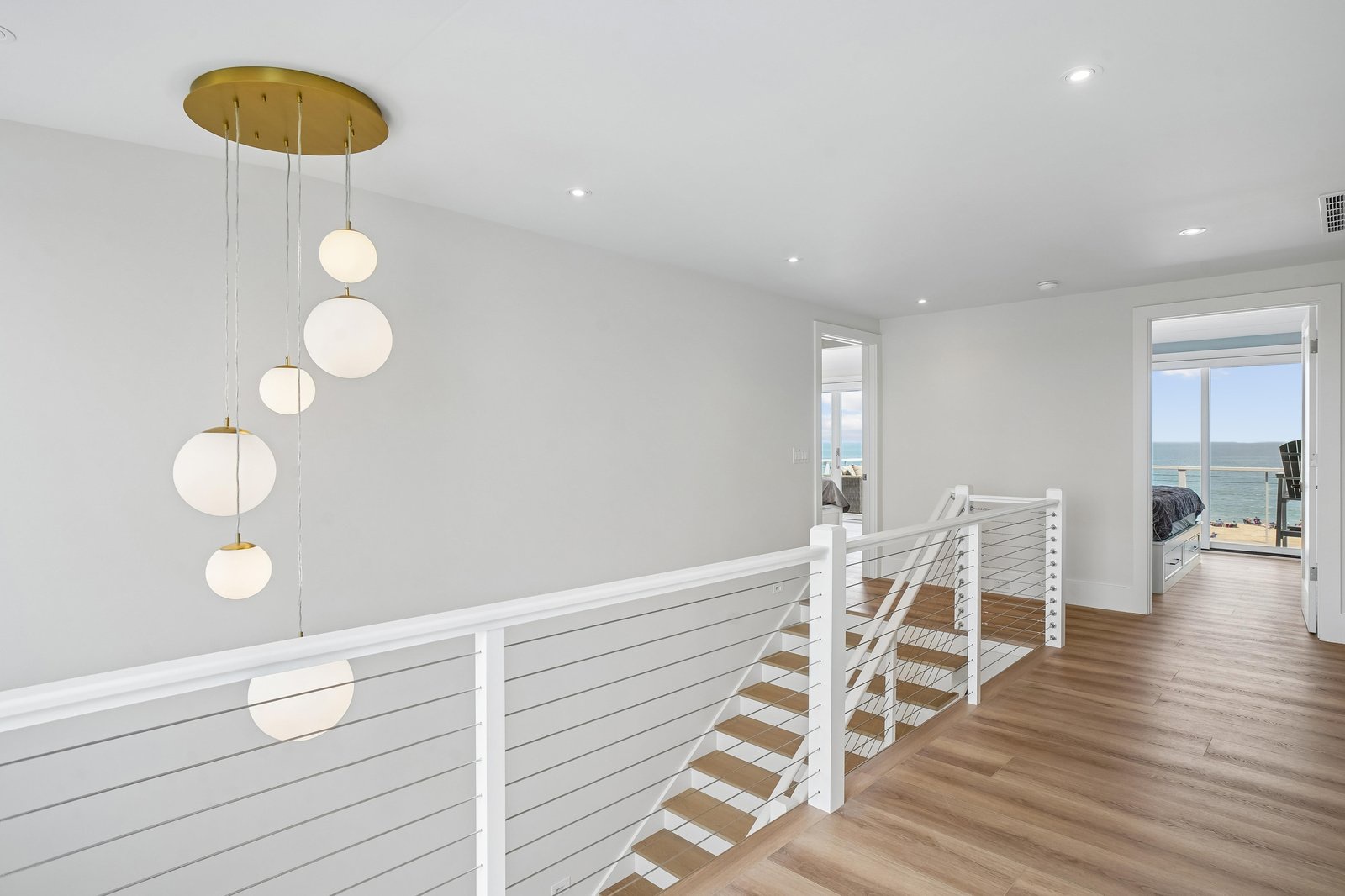 An airy upstairs hallway with modern lighting leads you toward ocean views through open doors—your seaside retreat awaits at every turn.