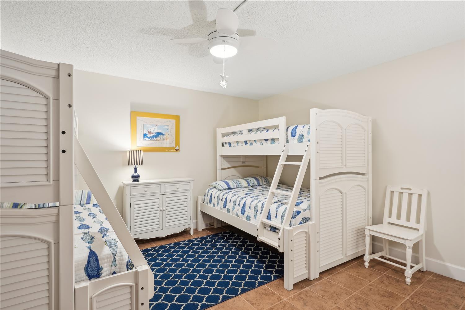 This cheerful bedroom welcomes your family with coastal-themed bunk beds and nautical accents. A ceiling fan keeps everyone cool while blue and white linens add beachy charm.