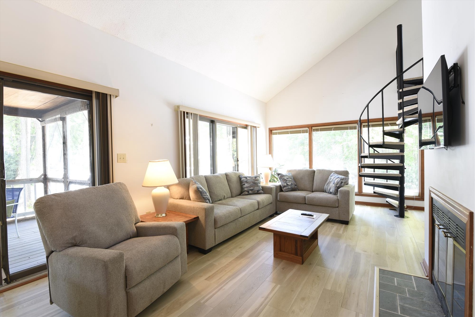 Settle into your spacious living room with plush gray seating, warm wood accents, and natural light streaming through large windows.