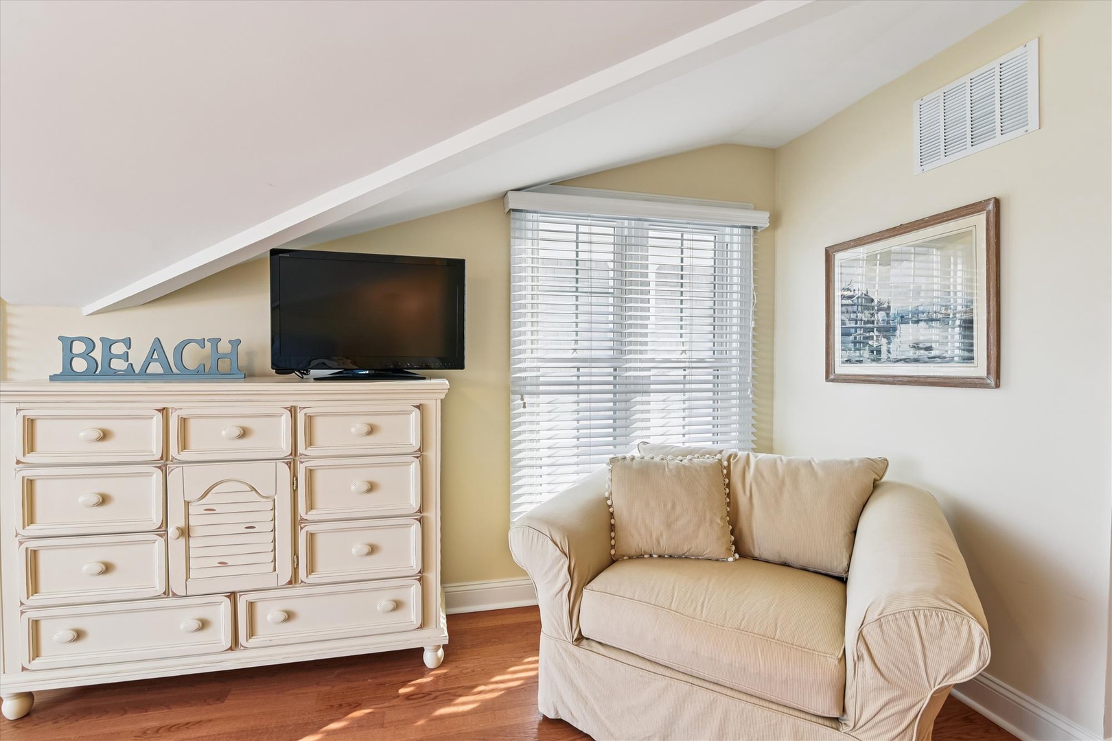 Soft sunlight streams through the windows, warming the cozy seating area with beachy charm. Your retreat includes a plush loveseat, entertainment setup, and coastal-inspired décor that sets the tone for relaxation.