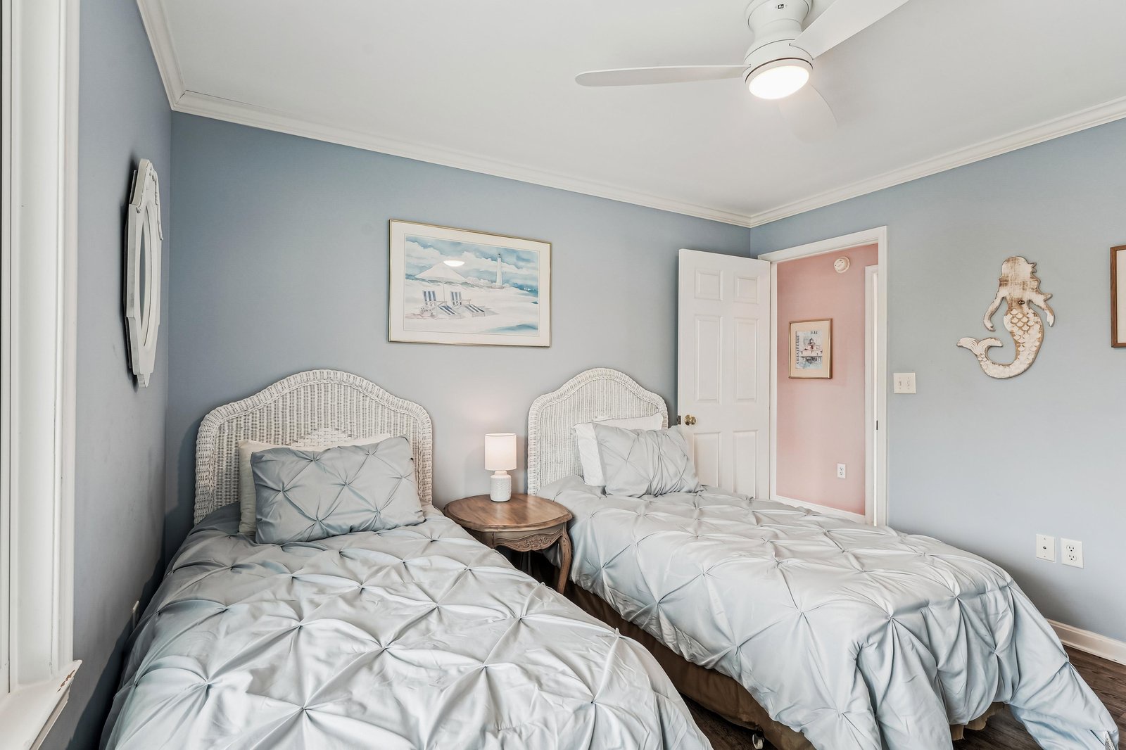 Your coastal retreat awaits in this serene bedroom, where two comfortable twin beds feature soft, textured linens beneath a bright ceiling fan. Charming nautical touches bring the beach indoors for a restful night.