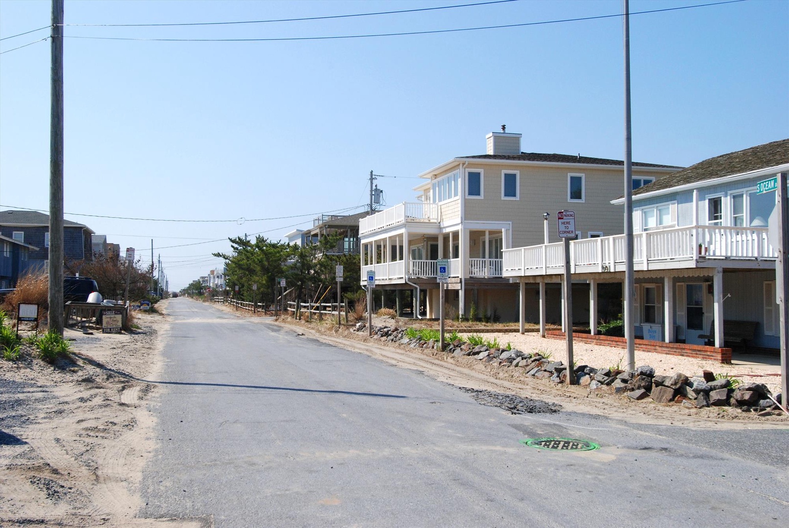 A coastal street view showcases the rental property nestled among beach houses, with convenient street parking and easy access to the sandy shore just steps away.