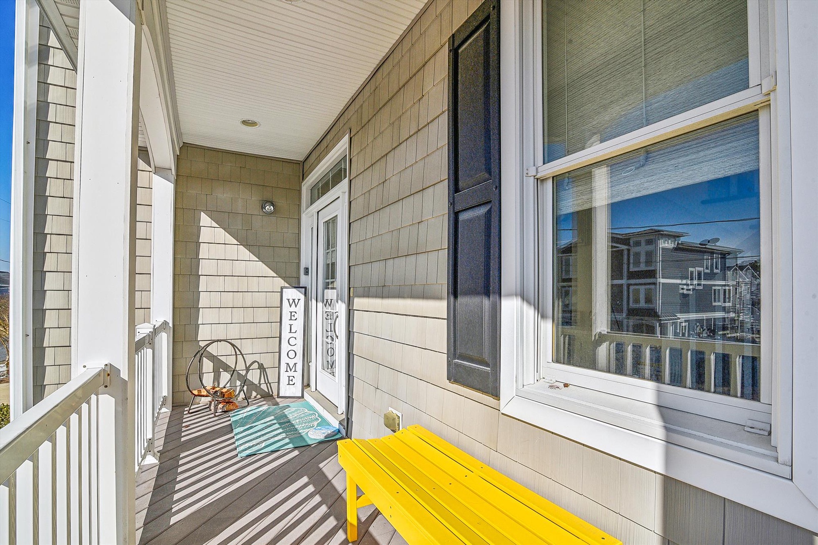 A cheerful bright yellow bench awaits you on this sunny porch entrance, where nautical decor and a welcoming sign greet your arrival at this charming coastal property.