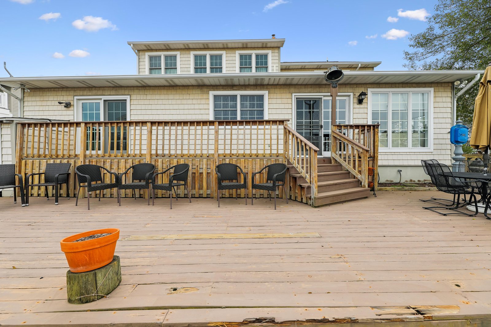 This coastal property features a spacious wrap-around deck with ample seating, offering an ideal spot for outdoor gatherings and waterside relaxation under sunny skies.