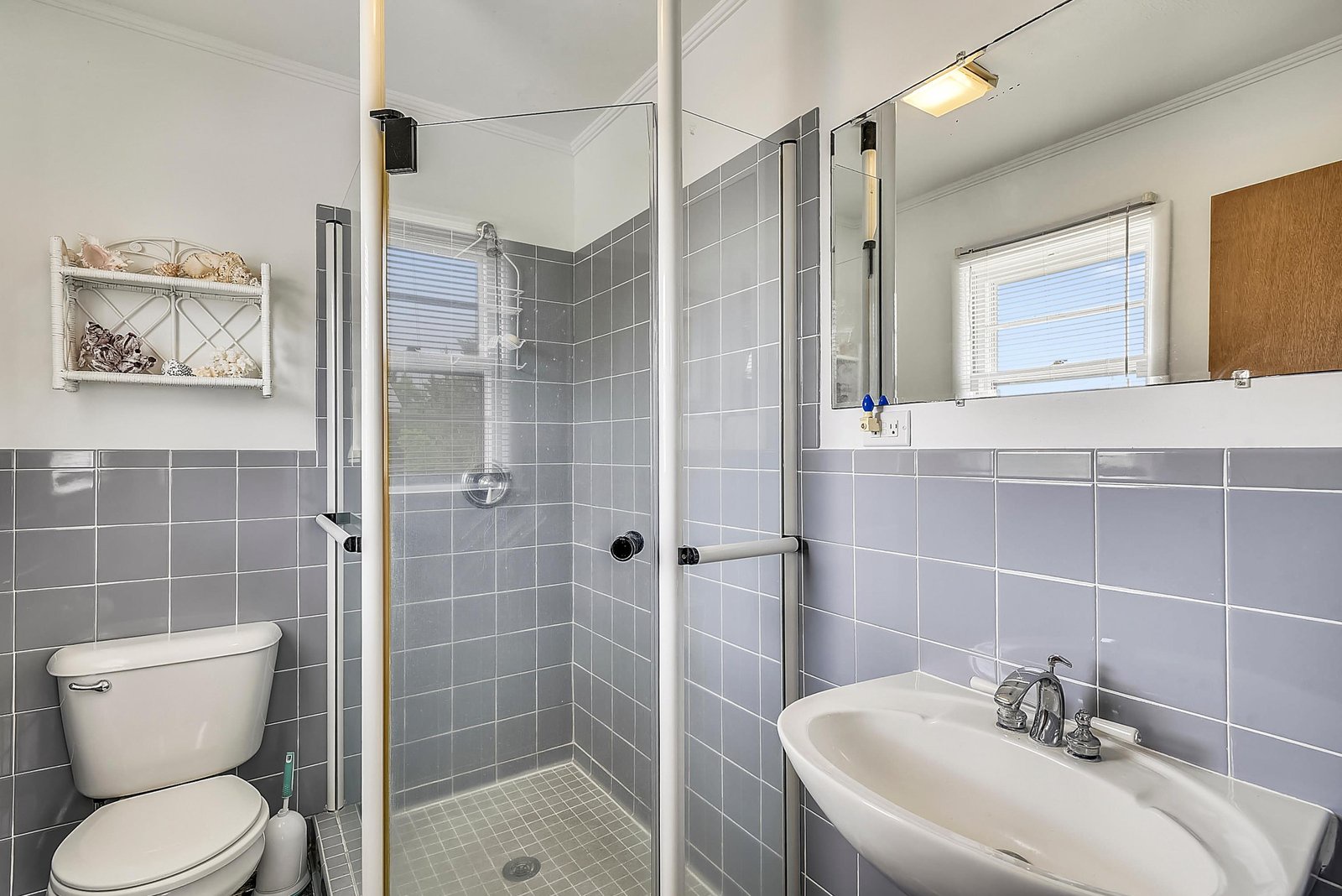 A coastal-inspired bathroom with soft gray tile and a spacious walk-in shower awaits your arrival. The bright window and beachy accents create a serene space to refresh after your day.