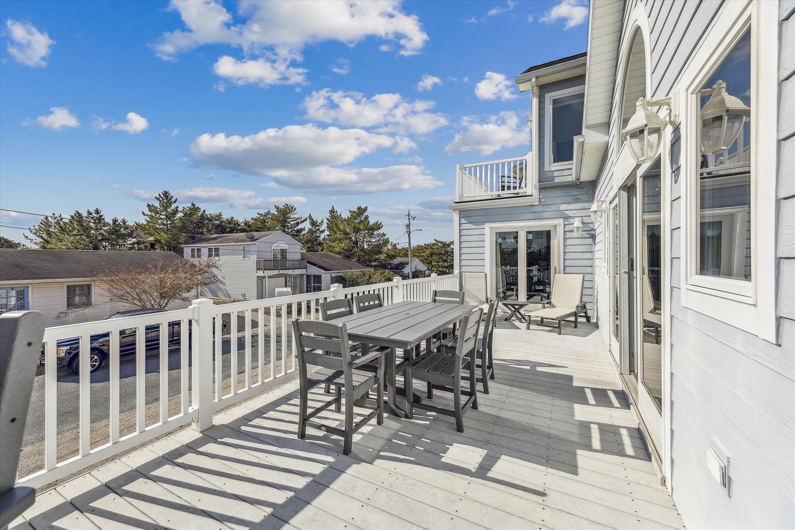A spacious deck with outdoor dining table and chairs, offering a serene coastal neighborhood setting for meals and gatherings under blue skies.