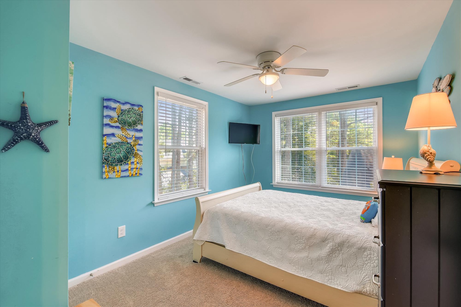 Drift off in your bright coastal bedroom with sea turtle art, ocean-inspired colors, and natural light streaming through blinds to greet you each morning.