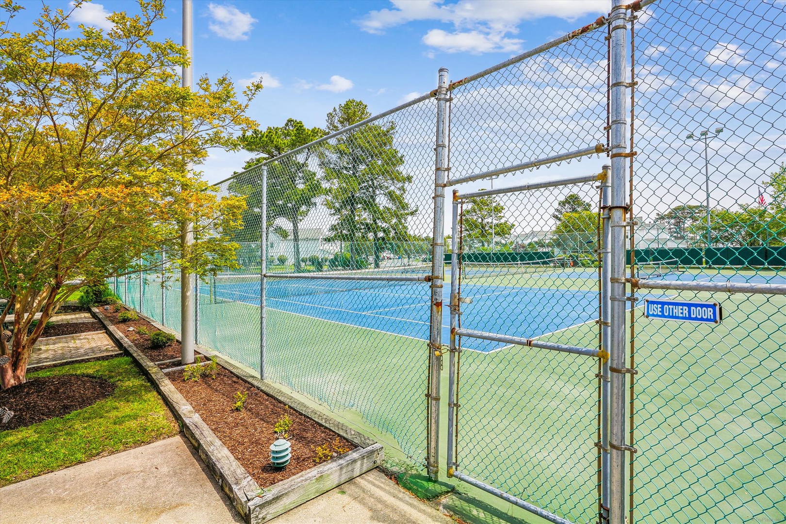 Step onto the tennis court for an active game surrounded by lush landscaping and blue skies.