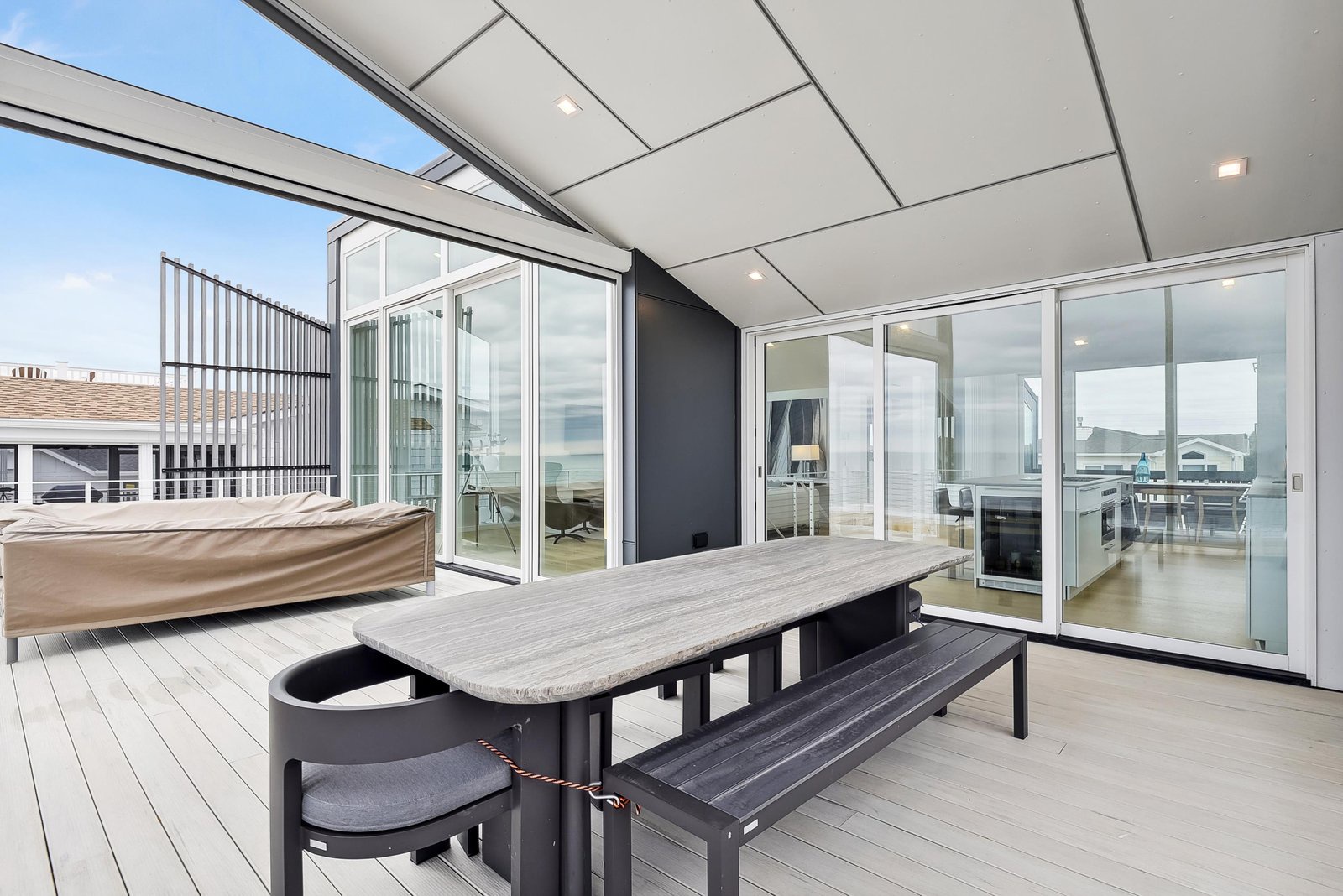 A modern rooftop terrace with sleek dining furniture and glass doors opening to bright interiors, offering a stylish open-air space for your meals and relaxation.
