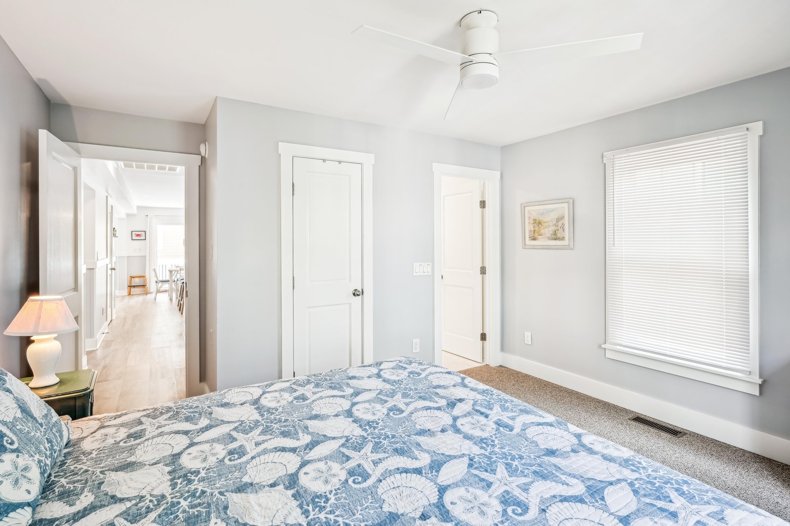 Drift off to sleep beneath the gentle hum of your ceiling fan in this serene bedroom, where soft coastal bedding and calming gray tones invite you to unwind after a day of seaside adventures.