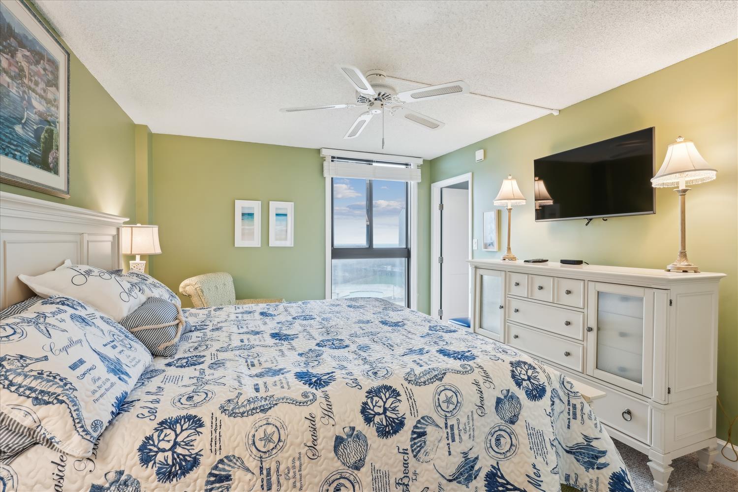 Sink into coastal comfort with breezy nautical bedding, a ceiling fan overhead, and glimpses of the ocean just beyond your balcony door, inviting you to unwind completely.
