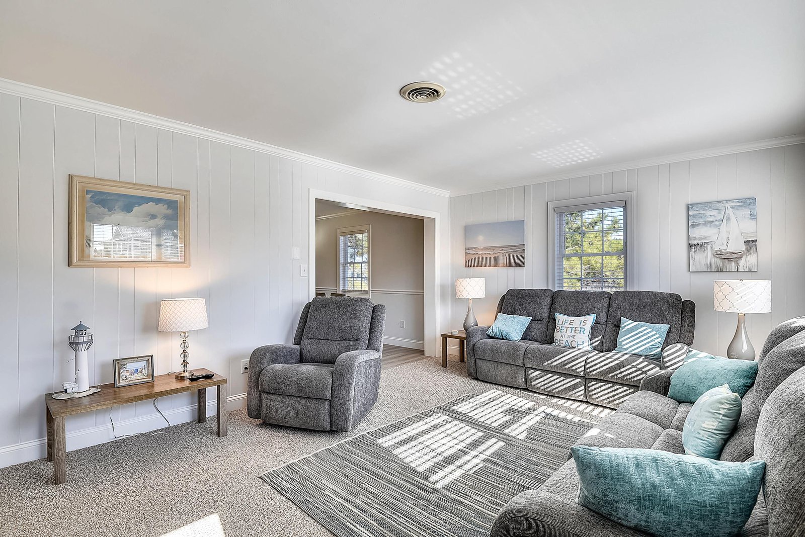 Settle into your spacious living room with plush reclining seating and coastal-inspired touches. Natural light streams through the window, perfect for your relaxing retreat.