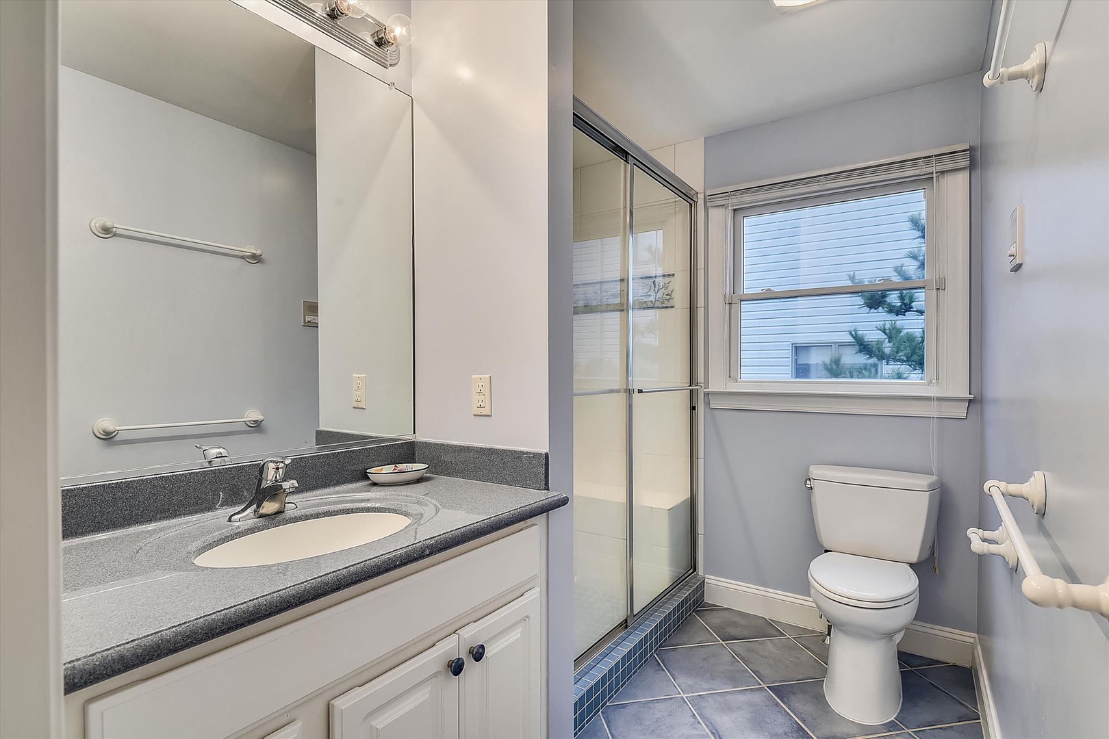 Step into your own clean, modern bathroom with a refreshing walk-in shower and plenty of natural light streaming through the window. You'll appreciate the thoughtful grab bars ensuring safe, easy movement around the space.